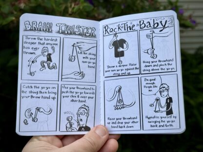 A hand holding open the Little Book Of Yo-Yo comic book. It shows the art and silly writing. Each page has black and white hand drawn art by Doc Pop.