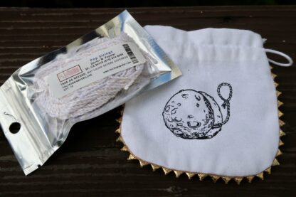 A plastic bag of yo-yo string. The string is white with a tiny gold thread throw it. The label looks like a pharmaceutical label with warnings like "take as needed". Behind the string is a cotton yo-yo bag with a logo printed on it. The logo is yo-yo that also looks like a moon.