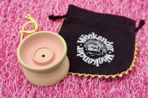 A cerakote Weekender on a pink surface. The yo-yo is on it's side and it's color is sort of pink with green highlights.